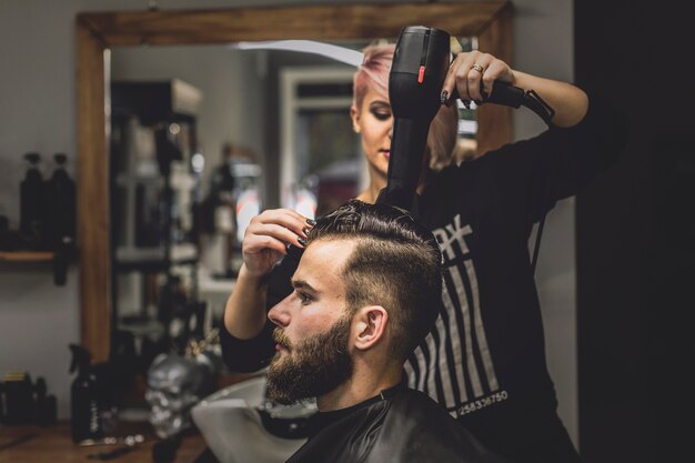 Kobieta suszarniczy włosy mężczyzna w zakładzie fryzjerskim