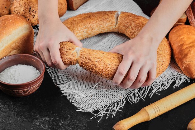 Kobieta Trzyma Bajgla Na Ciemnym Stole Z Różnymi Chlebami.