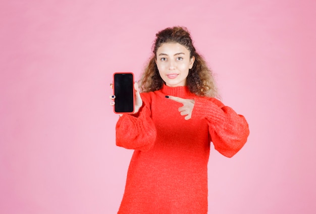 Bezpłatne zdjęcie kobieta trzyma i wskazuje na jej nowy smartfon marki.