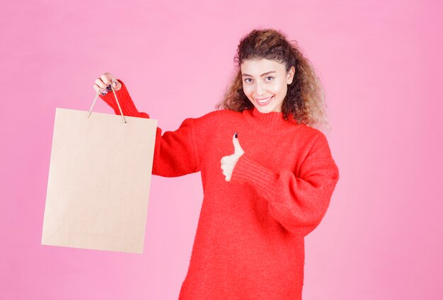 kobieta trzyma kartonową torbę na zakupy i pokazując kciuk do góry.