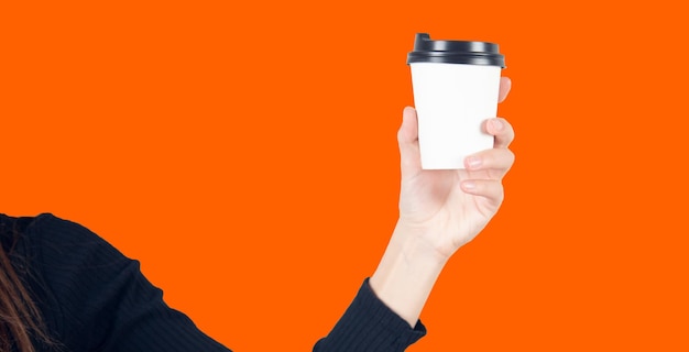 Kobieta trzyma papierową filiżankę kawy na pomarańczowym tle ściany