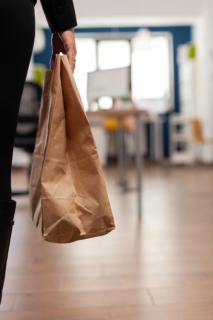 Kobieta trzyma papierową torbę z zamówieniem posiłku na wynos, kładąc na biurku podczas lunchu na wynos w biurze firmy