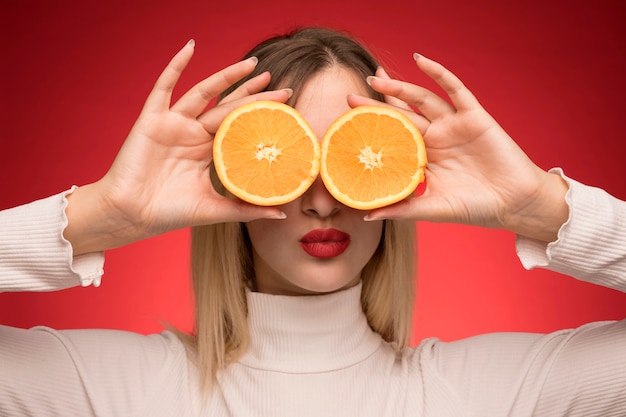 Kobieta trzyma plasterki pomarańczy nad jej oczami