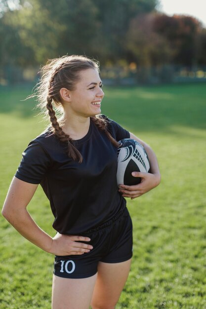 Kobieta trzyma rugby piłkę i patrzeje daleko od