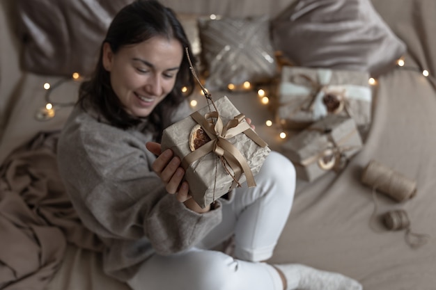 Kobieta trzyma świąteczne pudełko ozdobione w rzemieślniczym stylu, ozdobione suszonymi kwiatami i suchą pomarańczą, zawinięte w papier rzemieślniczy.