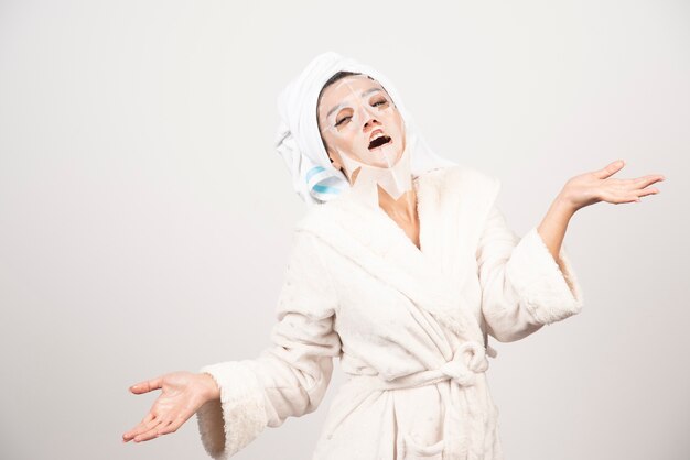 Kobieta ubrana w szlafrok i ręcznik z maską na twarz.