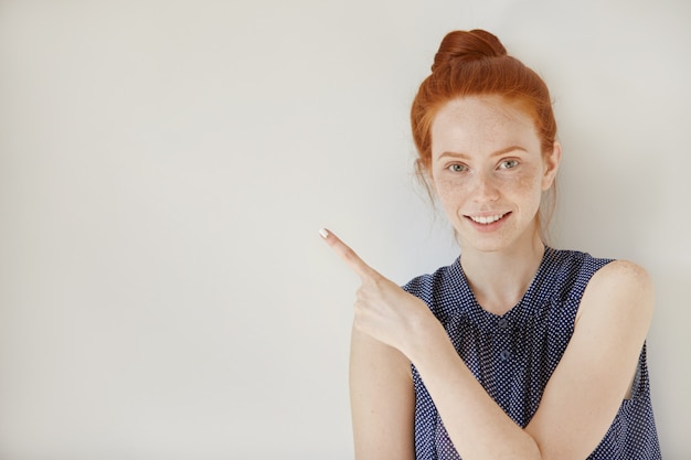Bezpłatne zdjęcie kobieta uśmiecha się radośnie i wskazuje jej palec wskazujący w górę