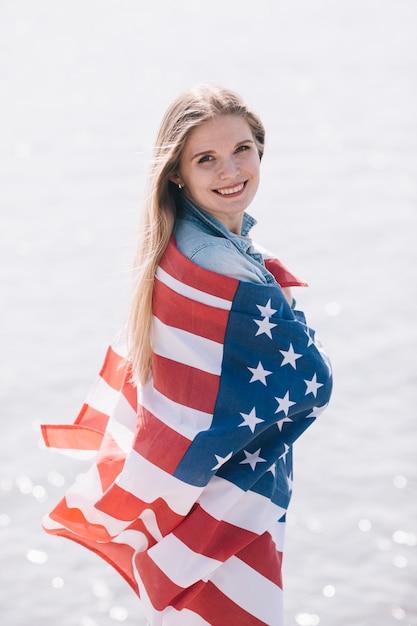 Bezpłatne zdjęcie kobieta uśmiechając się i patrząc na kamery owinięte w macha flagą amerykańską