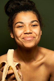 Kobieta Uśmiechająca Się Do Kamery, Trzymająca I Jedząca Dojrzałego żółtego Banana Odizolowanego Na Zielono Darmowe Zdjęcia