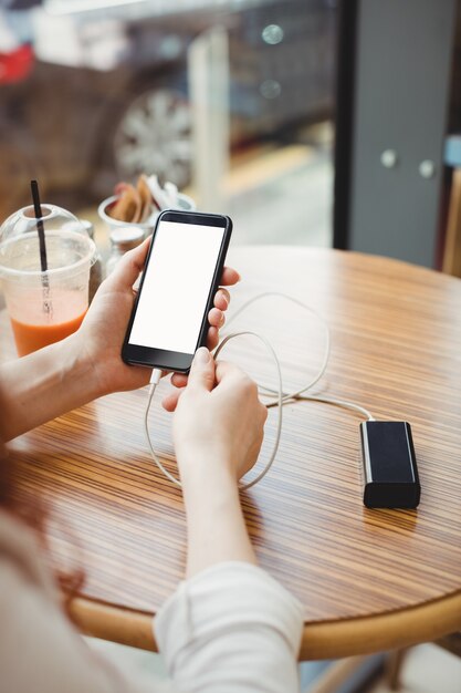 Kobieta używa przenośnego banku mocy do ładowania swojego telefonu w stołówce