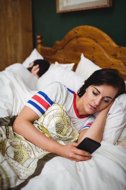 Kobieta używa telefon komórkowego podczas gdy kłamający na łóżku