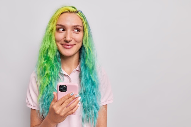 kobieta używa telefonu komórkowego do rozmów online ma długie, kolorowe włosy, korzysta z wiadomości w aplikacji lub robi zakupy, ubrana swobodnie, odizolowana na szaro
