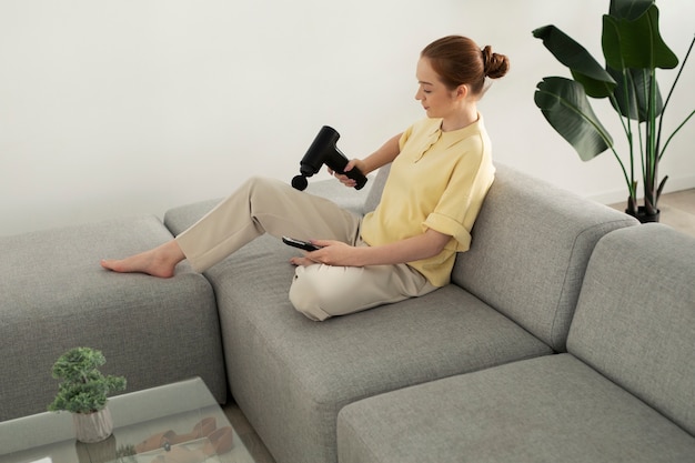 Bezpłatne zdjęcie kobieta używająca pistoletu do masażu do pełnego ujęcia nogi