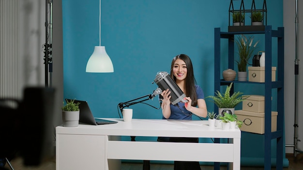 Kobieta vlogerka robi lekką rekomendację przed kamerą w studio, nagrywając podcast na żywo dla odbiorców mediów społecznościowych. Blogger korzystający ze studyjnego sprzętu oświetleniowego do sprawdzania produktu w strumieniu kanału.