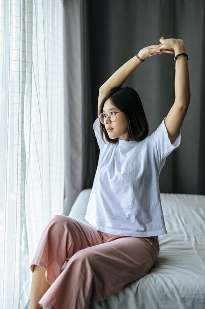 Kobieta w białej koszuli siedząca na łóżku i podnosząca obie ręce.