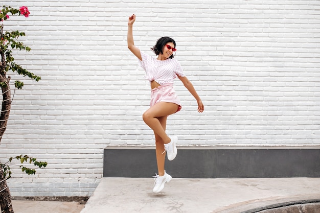 kobieta w białych trampkach, skoki na ulicy. Pełny widok długości tańczącej kobiety cieszącej się latem.