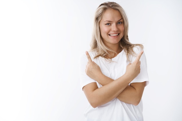 Bezpłatne zdjęcie kobieta w białym t-shircie skrzyżowane ramiona skierowane bokiem w górne rogi uśmiechnięte pozytywnie sugerujące wybór wariantów