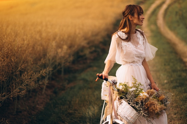 Kobieta w biel sukni z bicyklem w polu