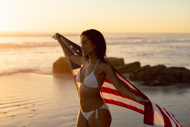 Kobieta w bikini trzyma flaga amerykańską na plaży