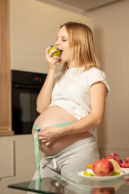 Kobieta w ciąży je jabłka i mierzy jej brzucha