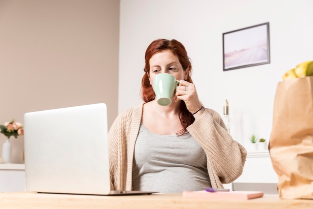 Kobieta w ciąży patrzeje na laptopie w domu