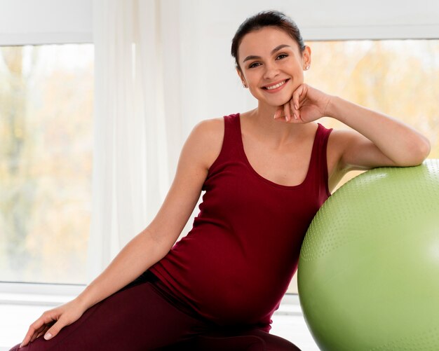 Kobieta w ciąży pozuje obok piłki fitness