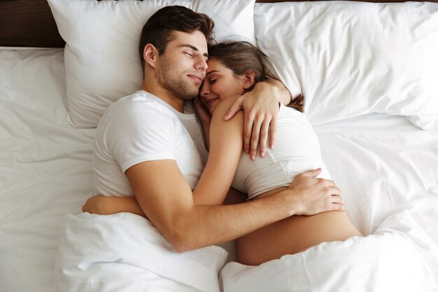 Kobieta w ciąży śpi w łóżku z mężem