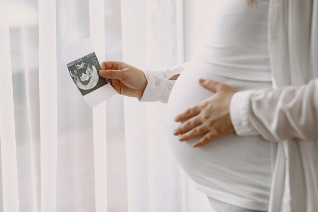 Kobieta w ciąży stojąca przy oknie patrząc na zdjęcie.