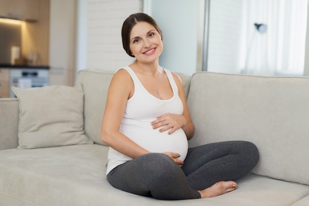 Kobieta w ciąży trzyma ręce na brzuchu i uśmiecha się.