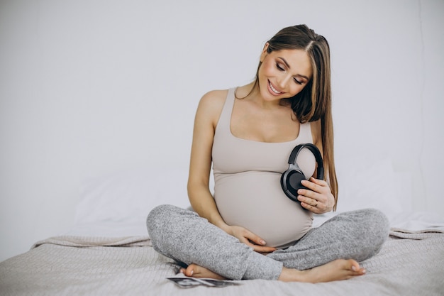 Kobieta w ciąży ze zdjęciem USG zakładająca na brzuch słuchawki z muzyką