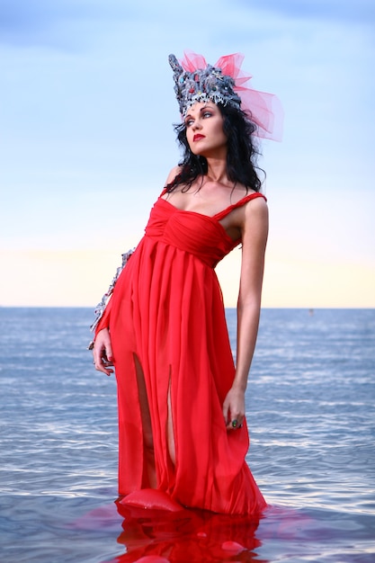 Kobieta w czerwonej awangardowej sukni na plaży w wodzie
