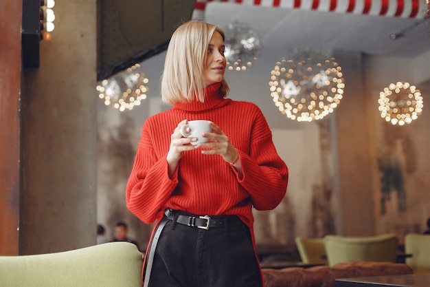 Kobieta w czerwonym swetrze. Pani pije kawę.