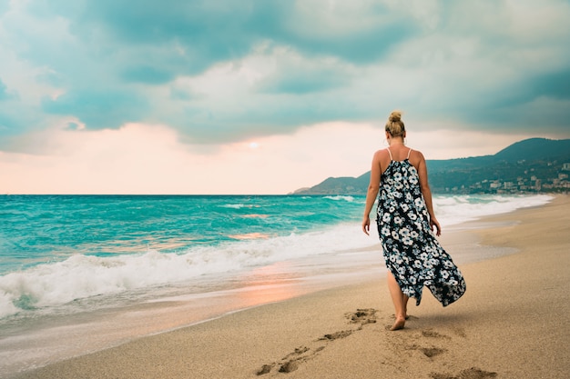 Kobieta w długiej sukni spaceru nad brzegiem morza