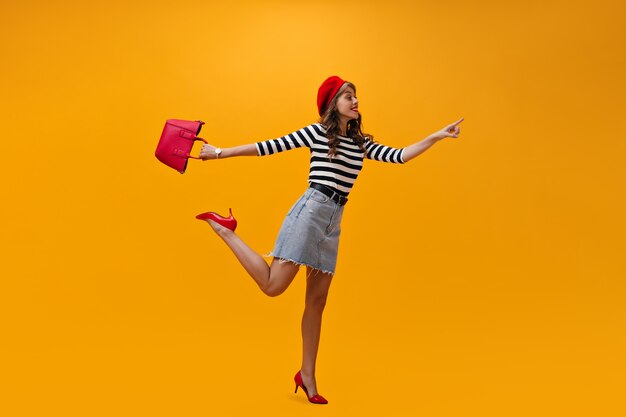Kobieta w dobrym nastroju, wskazując miejsce na tekst na pomarańczowym tle. Uśmiechający się modna dziewczyna w paski sweter i czerwone obcasy pozowanie.