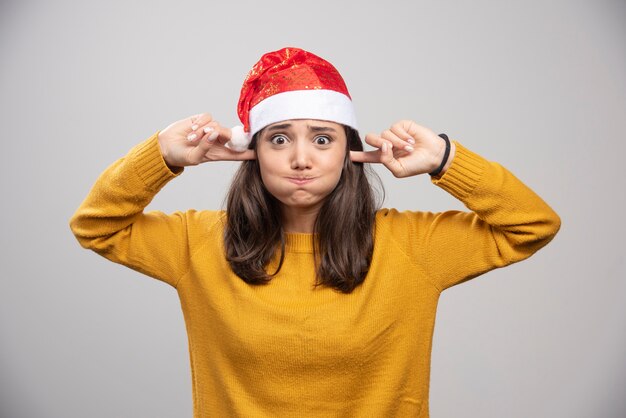 Kobieta w kapeluszu Santa zakrywająca uszy i wstrzymująca oddech.