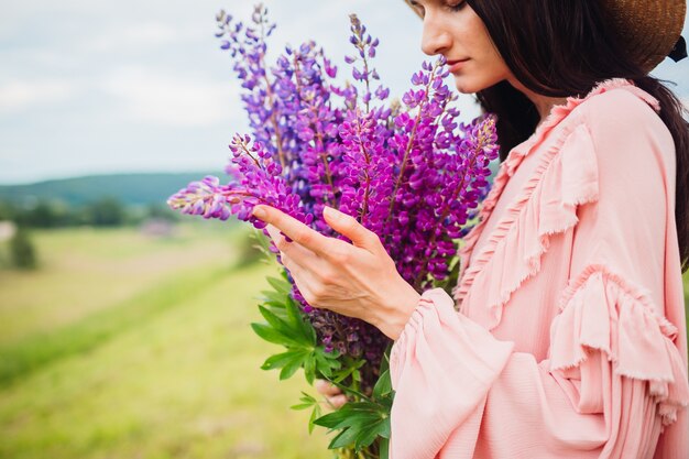 Kobieta w kapeluszu siana pozuje z bukietem lavander na polu