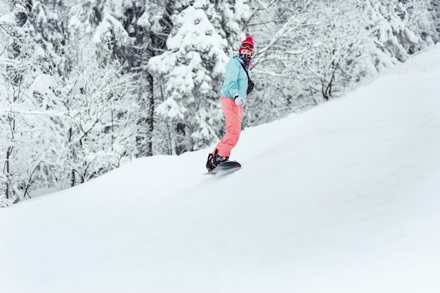 Kobieta w kombinezon narciarski wygląda na jej ramieniu schodząc ze wzgórza na jej snowboard