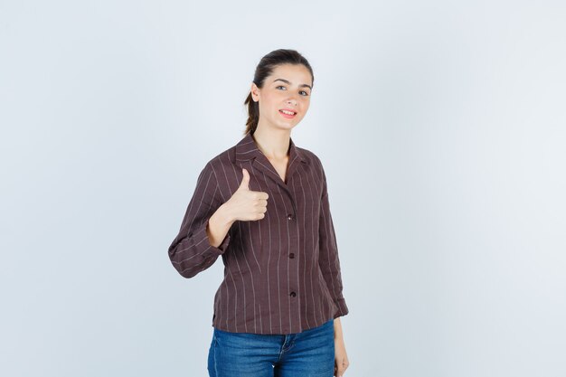 Kobieta w koszuli, dżinsy pokazując kciuk i patrząc szczęśliwy, widok z przodu.