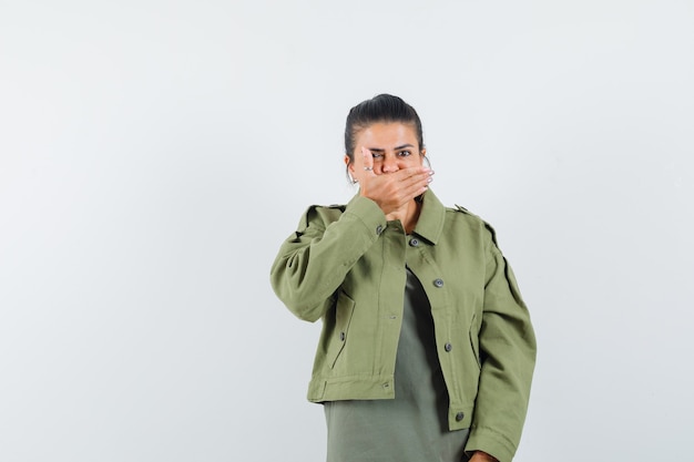 kobieta w kurtce, t-shirt, trzymając dłoń na ustach i wyglądająca na przestraszoną