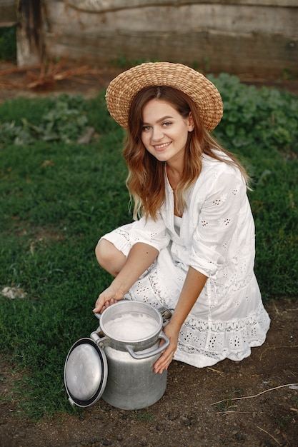 Bezpłatne zdjęcie kobieta w letnim polu. dziewczyna w białej sukni. kobieta z beczką mleka.