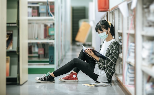 Kobieta w maskach siedzi i czyta książkę w bibliotece.