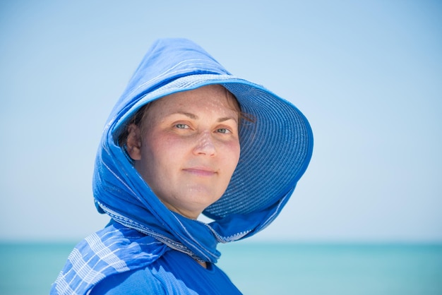 Kobieta w niebieskim kapeluszu na tle niebieskiego nieba i wody. koncepcja wakacji