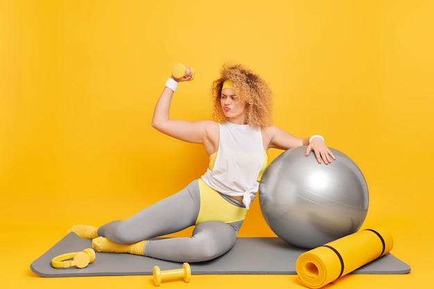 Kobieta W Odzieży Sportowej Podnosi Rękę Z Hantlami Trenuje Fitness Na Macie Używa Sprzętu Sportowego Będąc W Dobrej Formie Fizycznej