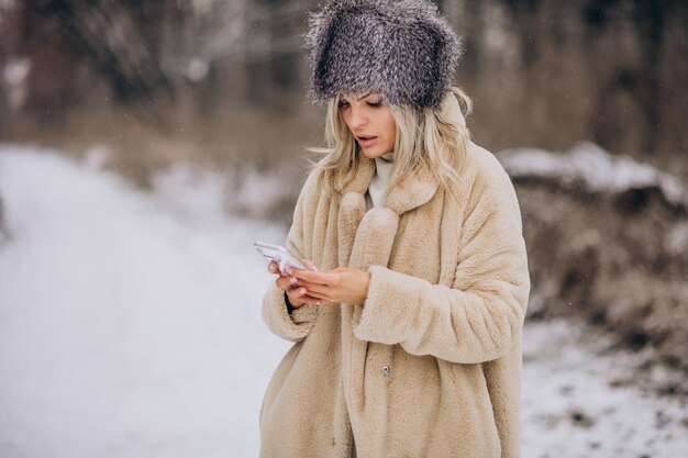 Kobieta w płaszczu zimowym spacerująca w parku pełnym śniegu rozmawiająca przez telefon