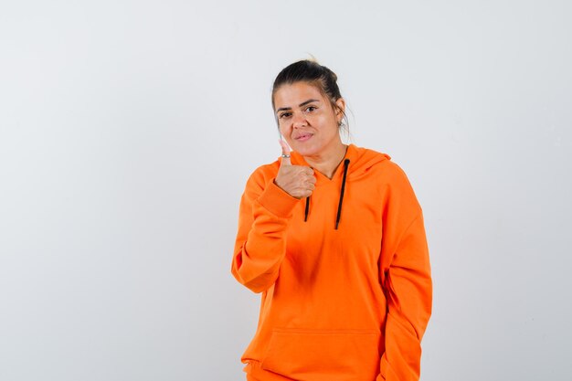 Kobieta w pomarańczowej bluzie z kapturem pokazująca kciuk w górę i wyglądająca pewnie
