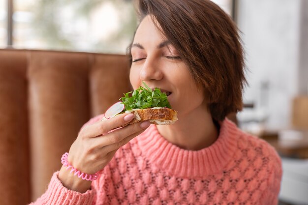 Kobieta w restauracji w przytulnym ciepłym swetrze pełnowartościowe śniadanie z tostami z rukolą i łososiem