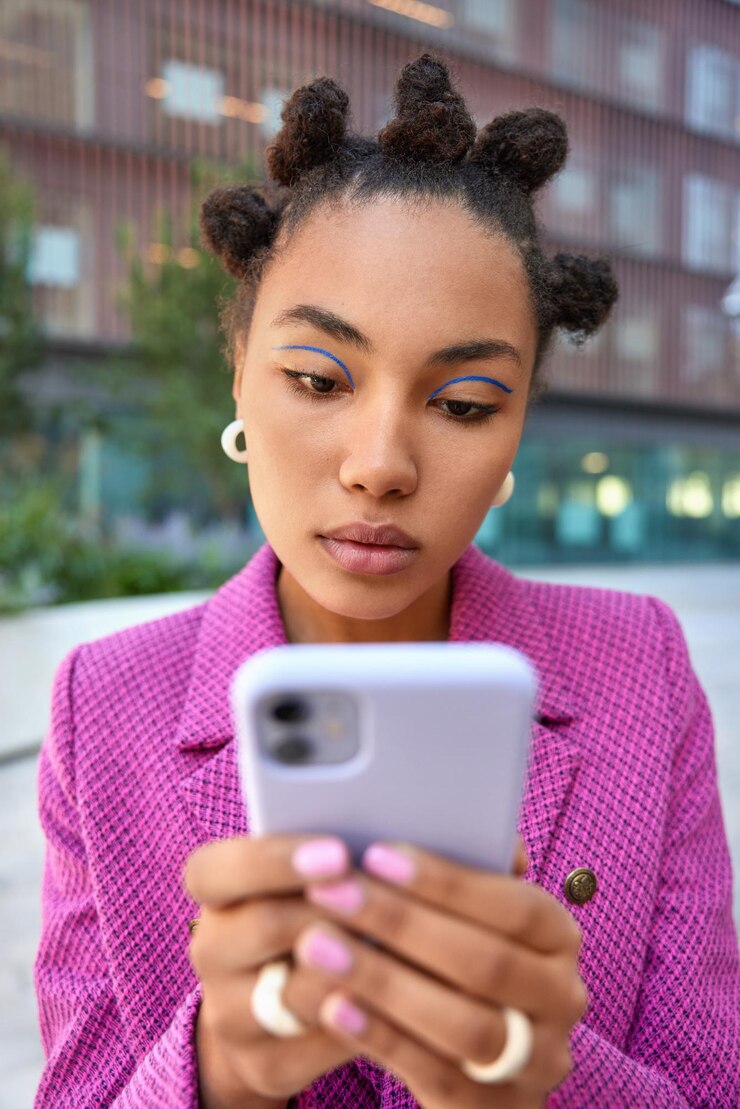 Bezpłatny plik Zdjęcie kobieta w różowej kurtce trzyma telefon komórkowy odczytuje odbieranie wiadomości spacery po ulicach sprawdza sieci społecznościowe. moda i technologia