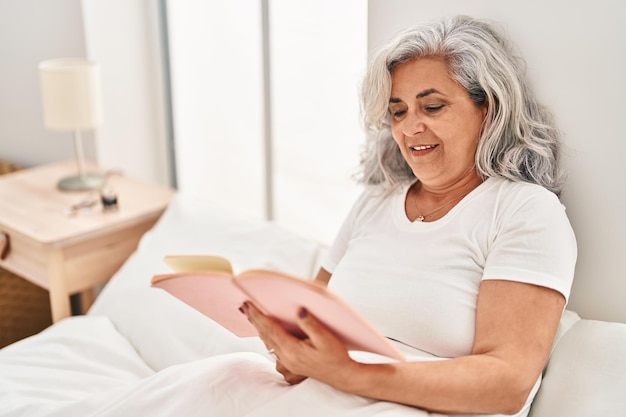 Bezpłatne zdjęcie kobieta w średnim wieku czytająca książkę siedząca na łóżku w sypialni