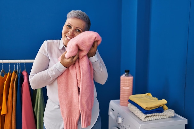 Kobieta w średnim wieku, uśmiechnięta, pewna siebie, dotykająca miękkiego swetra z twarzą w pralni