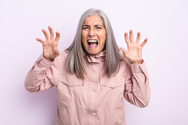 Kobieta w średnim wieku z siwymi włosami, krzycząca w panice lub złości, wstrząśnięta, przerażona lub wściekła, z rękami przy głowie